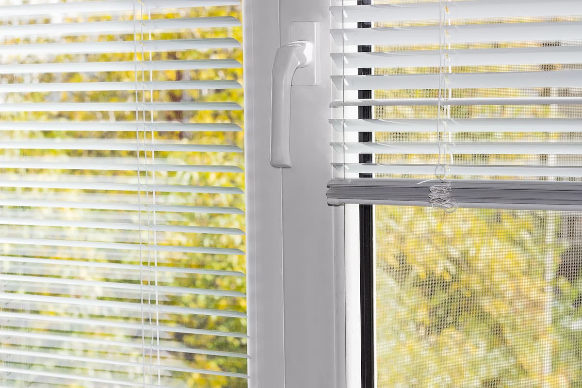 Fragmento de la moderna ventana de plástico con persianas venecianas blancas