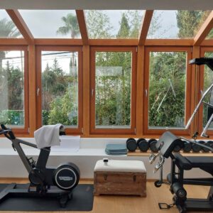 Gimnasio interior con grandes ventanas, mancuernas y otros equipos de entrenamiento.
